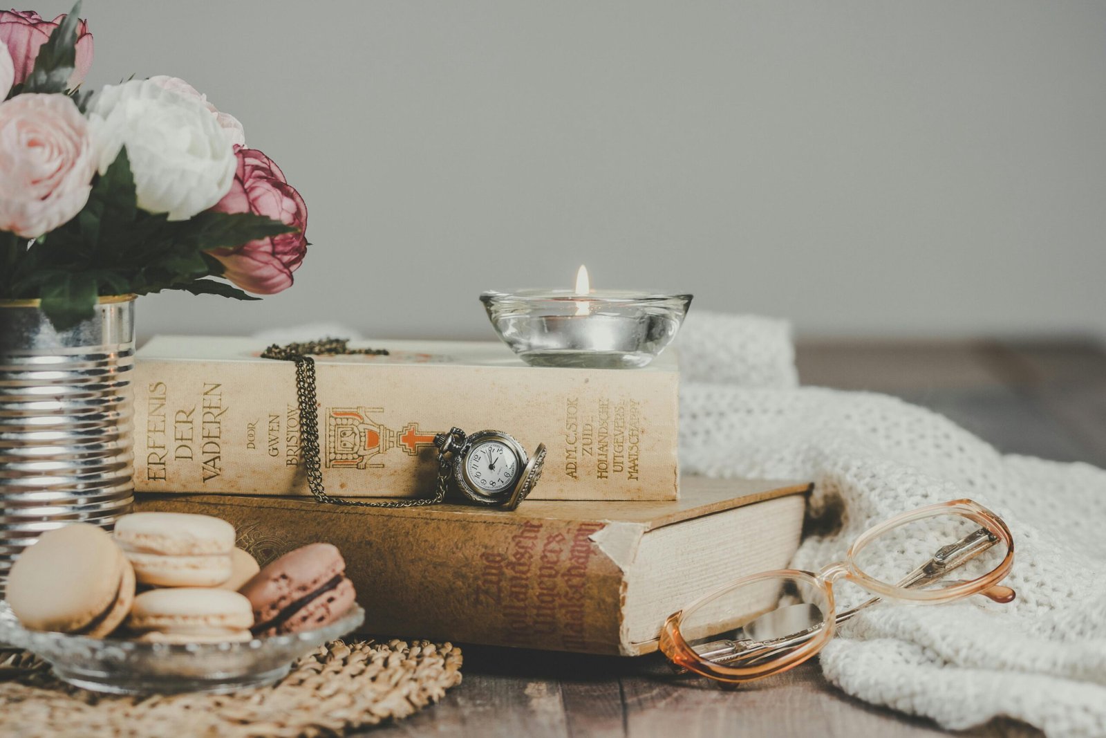 Vintage still life with books, macarons, candle, and flowers on a cozy table.